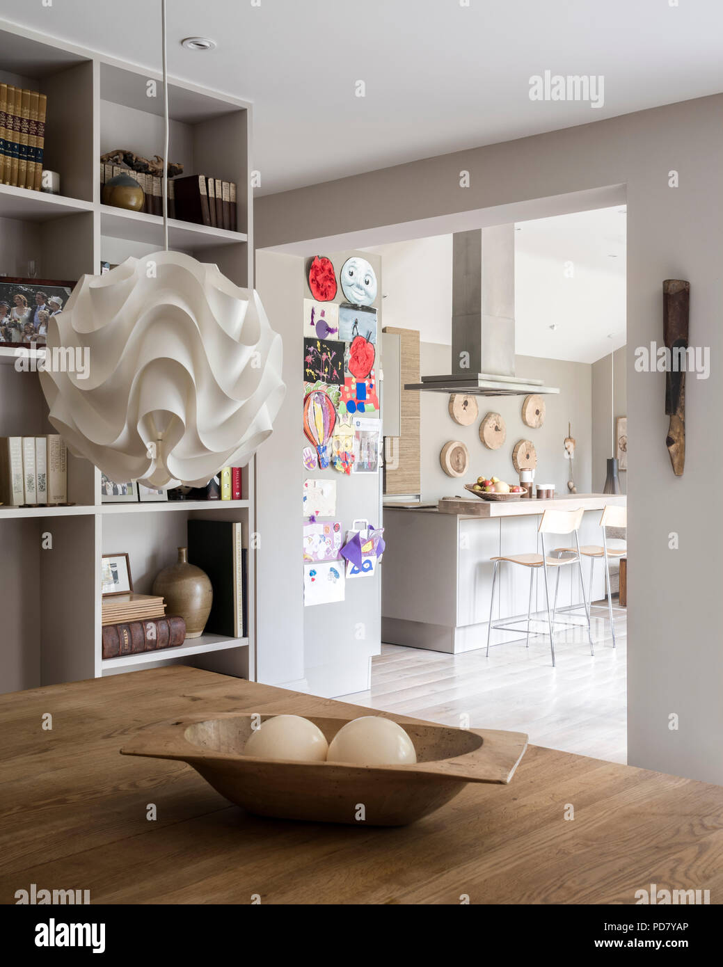 Paper pendant light by Skandium hangs above an oak dining table. In the background the kitchen is visible through a square arch Stock Photo