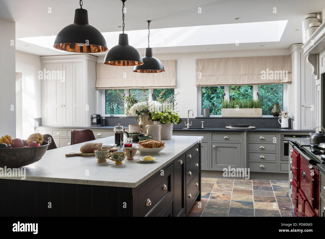 Bespoke kitchen island by Thomas Ford & Sons is painted in Tanner's Brown by Farrow & Ball. Industrial style pendant lights hang above Stock Photo