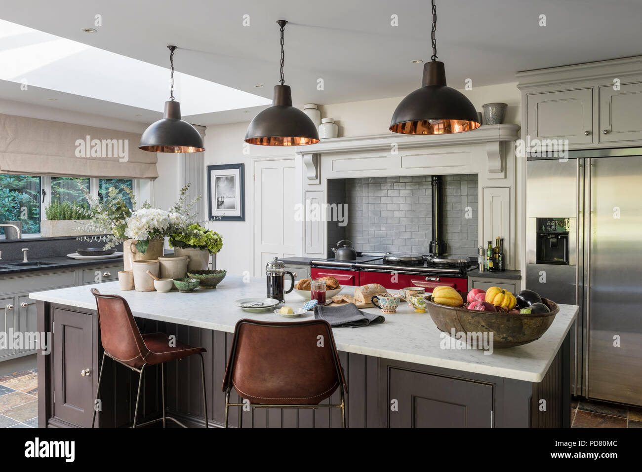 Bespoke kitchen island by Thomas Ford & Sons is painted in Tanner's Brown by Farrow & Ball. Industrial style pendant lights hang above and the bar sto Stock Photo