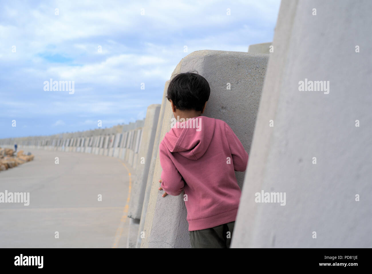 Playing hide and seek. Kid peeking from behind the wall outdoor. Child hiding behind wall. Stock Photo