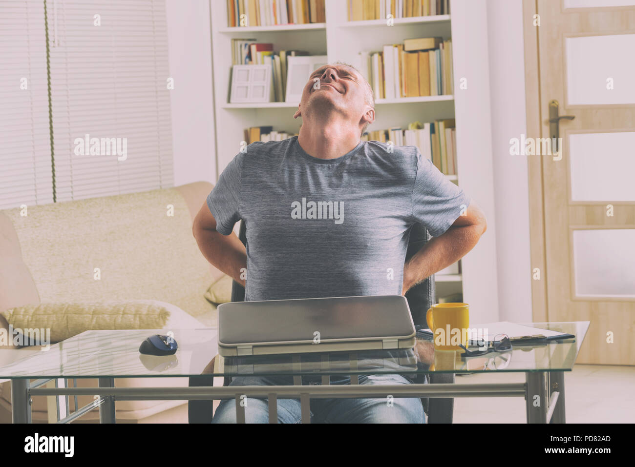 Man in home office suffering from low back pain sitting at a desk with