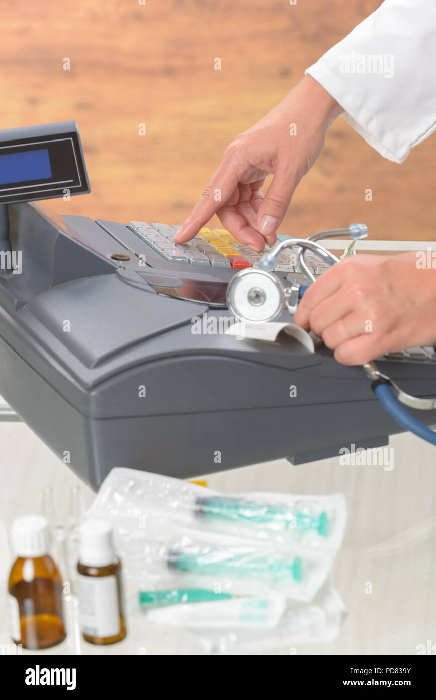 pharmacist or medical doctor holdnig stethoscope and using cash register at pharmacy or surgery