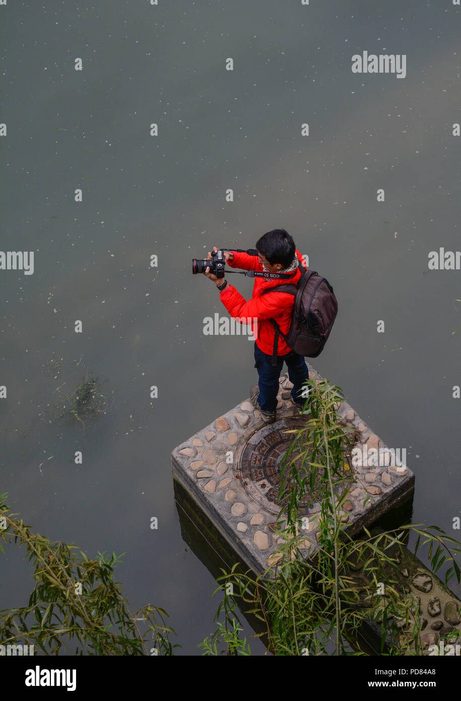 Hunan, China - Nov 5, 2015. A young man standing on riverbank and taking pictures at Fenghuang Ancient Town in Hunan, China. Stock Photo