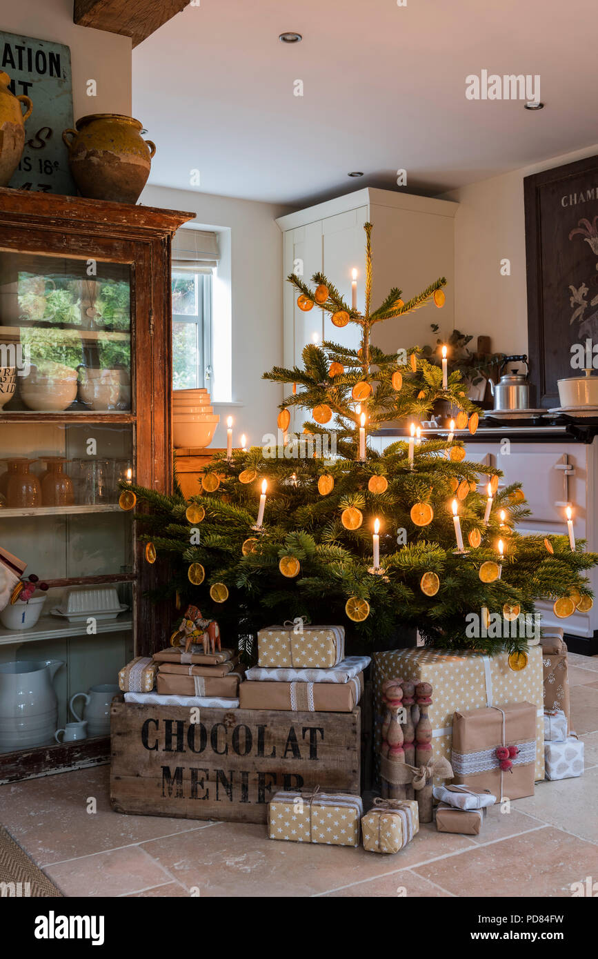 Candle lit christmas tree in cottage kitchen with wrapped presents Chocolat menier boxes Stock Photo