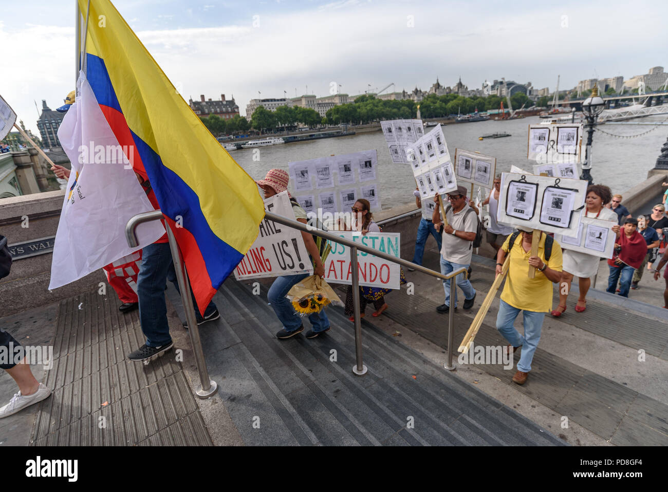 London, UK. 7th August 2018. Colombians and supporters of human rights walk up the steps to Westminster Bridge with posters, flowers and Colombian flags holding pictures of over a hundred murdered community leaders in support of the peace process in Colombia and demanding an end to the daily threats and murders throughout the country. Credit: Peter Marshall/Alamy Live News Stock Photo