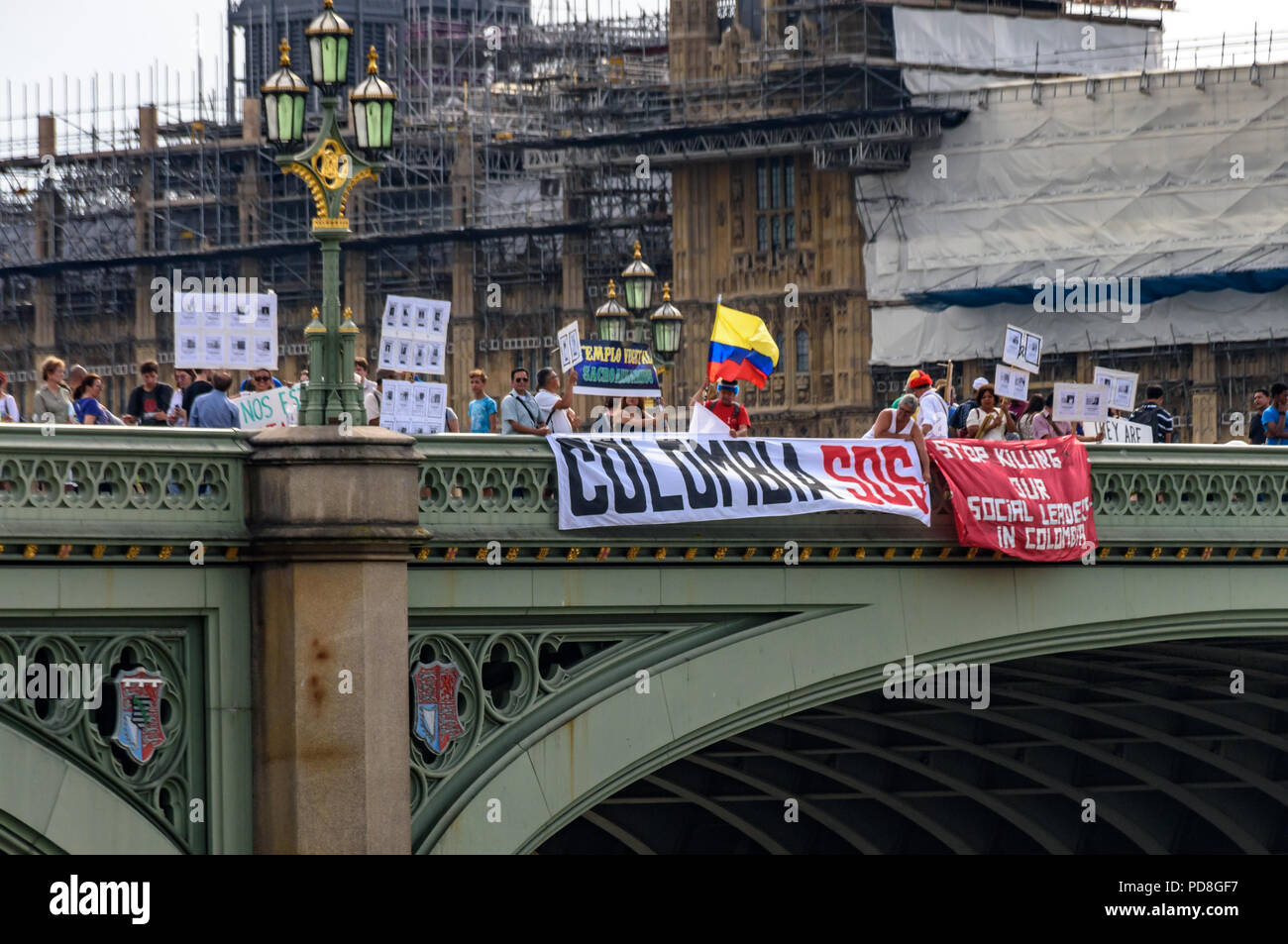 London, UK. 7th August 2018. Colombians and supporters of human rights drop banners over Westminster Bridge as they walk with flowers and Colombian flags holding pictures of over a hundred murdered community leaders to a protest in Parliament Square in support of the peace process in Colombia and demanding an end to the daily threats and murders throughout the country. The International Mobilization for Life and Peace called on the new President of Colombia to put into action an urgent plan to protect social leaders and rapidly implement the peace agreement. Similar actions in the Internationa Stock Photo