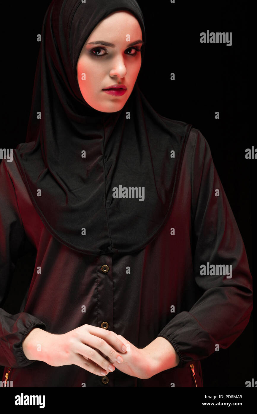 Portrait of beautiful arrogant young muslim woman wearing black hijab as conservative fashion concept with hand on hand on black background Stock Photo