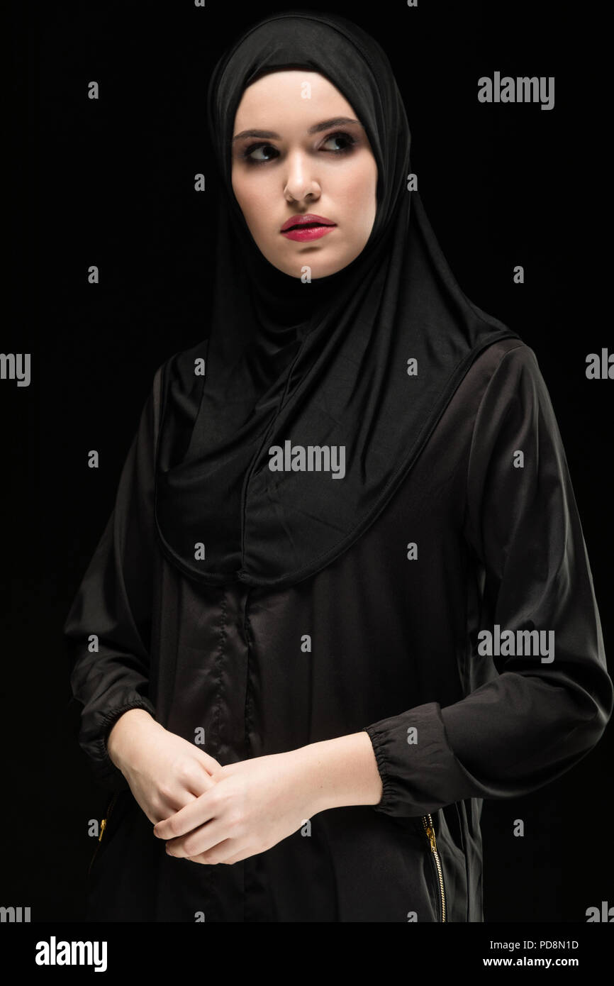 Portrait of beautiful confident young muslim woman wearing black hijab as conservative fashion concept on black background Stock Photo