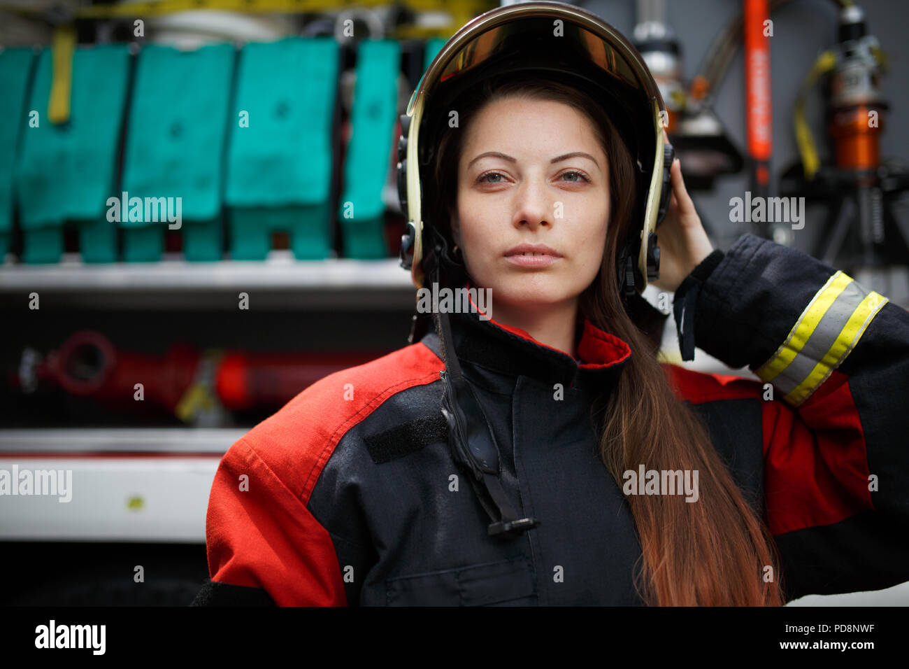 Photo of young fire woman with long hair in helmet looking into camera next to fire engine Stock Photo