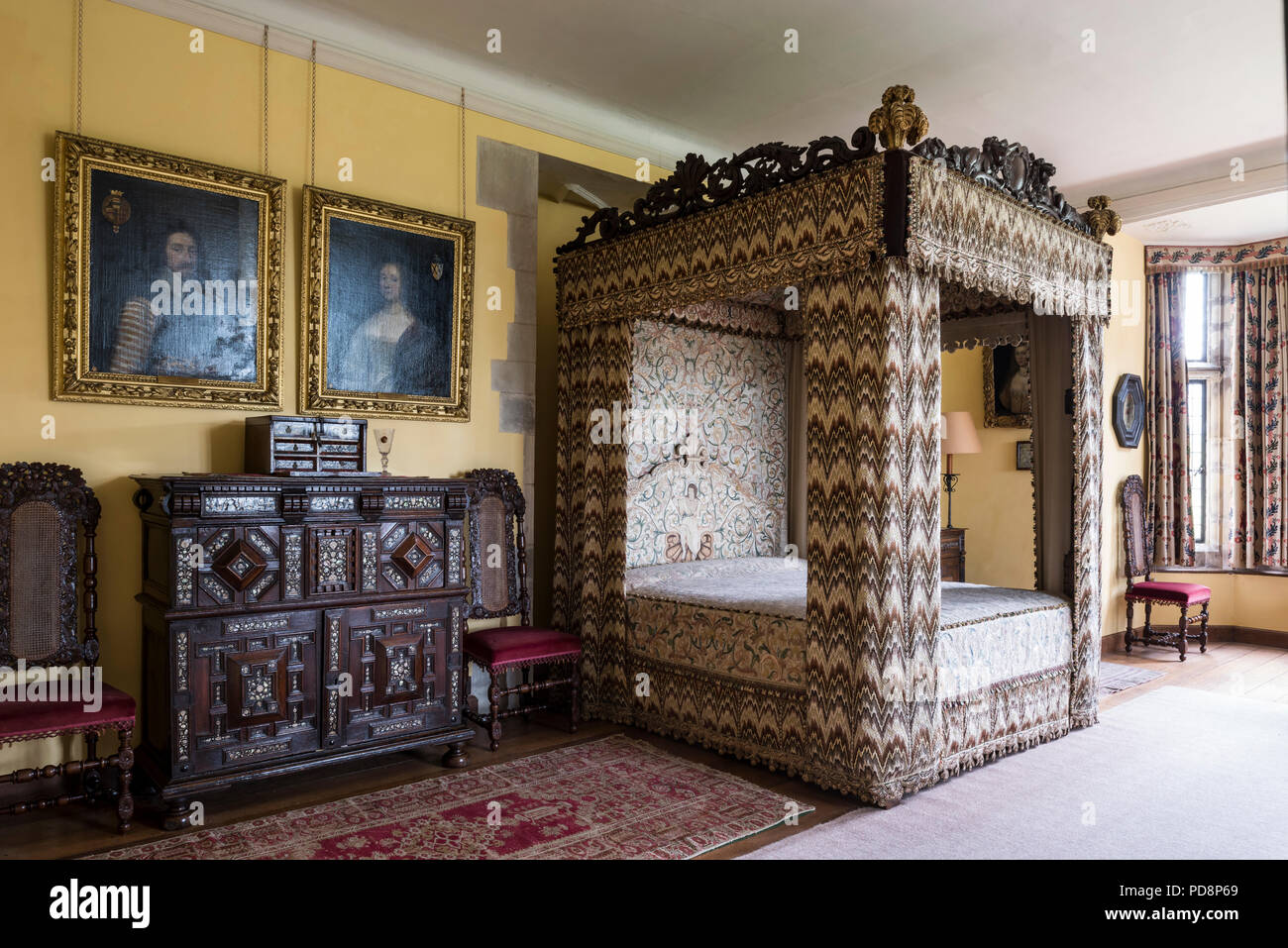 Four postered bed with  17th century flame stitch embroidery and gilt framed artwork above inlaid cabinet Stock Photo
