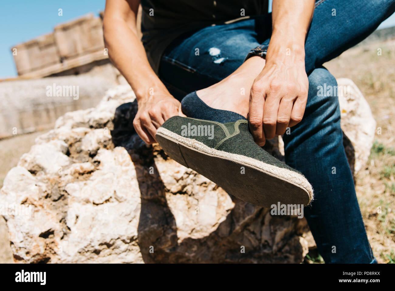 closeup of a young caucasian man sitting on a rock outdoors putting on or taking off his shoe, with a low cut sock on his foot Stock Photo