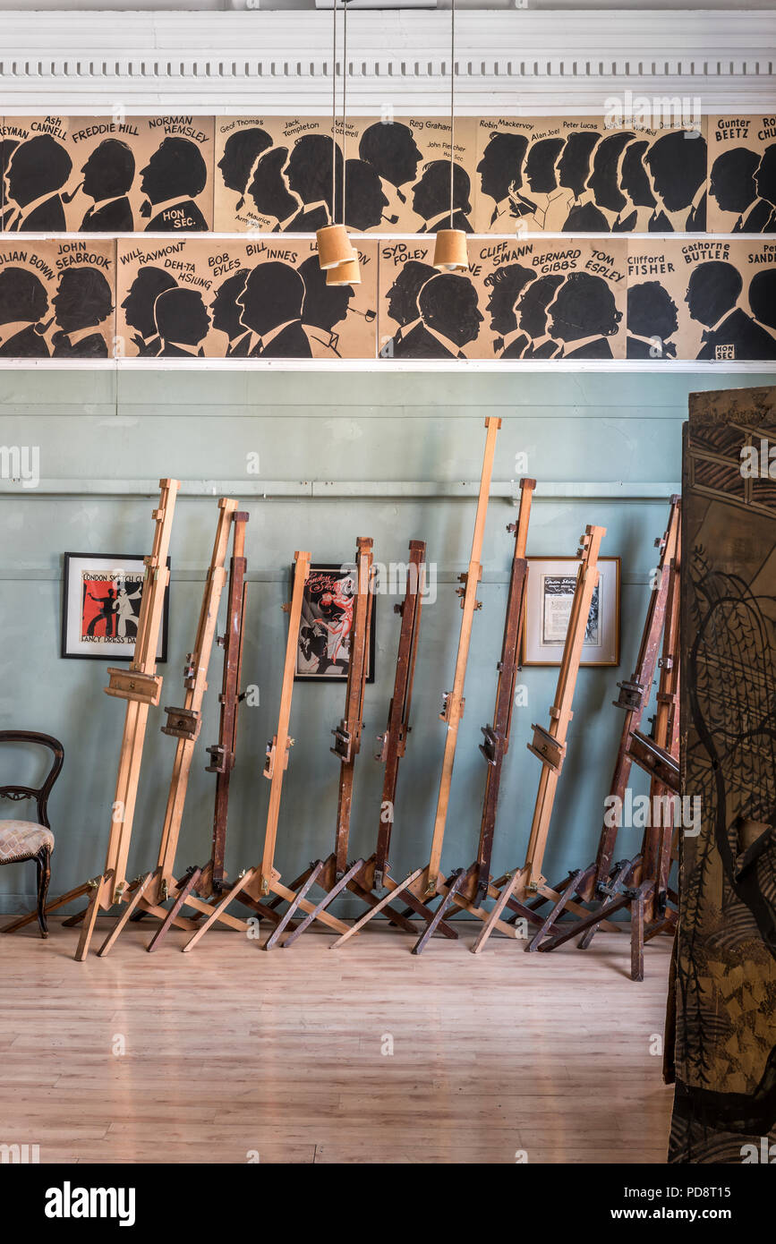 A stack of easels in the clubroom of the London Sketch Club. The silhouettes of past members adorn the wall above Stock Photo