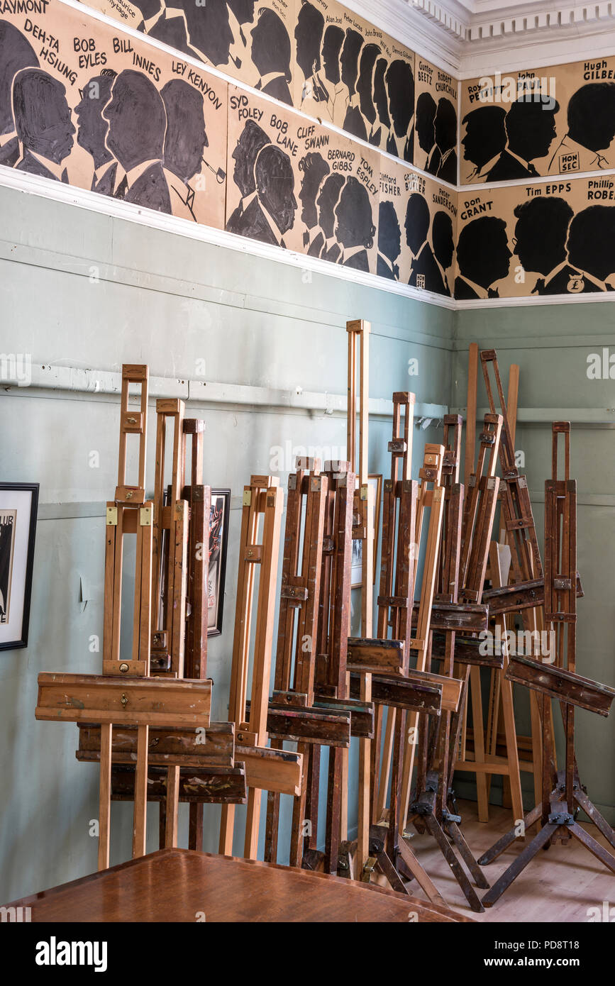 A stack of easels in the clubroom of the London Sketch Club. The silhouettes of past members adorn the wall above Stock Photo