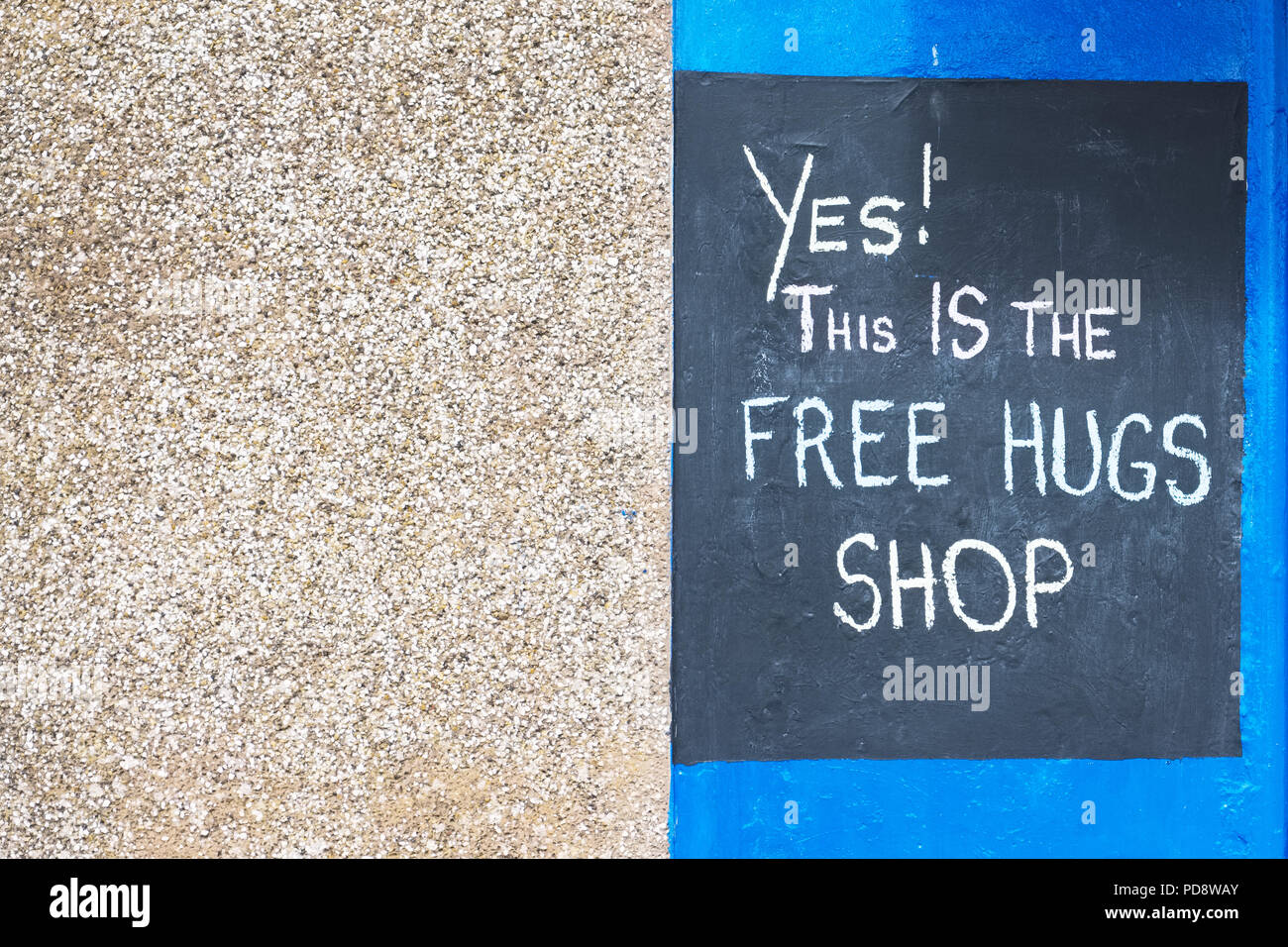 Free hugs sign on shop wall written in chalk on black board against neutral and blue background Stock Photo