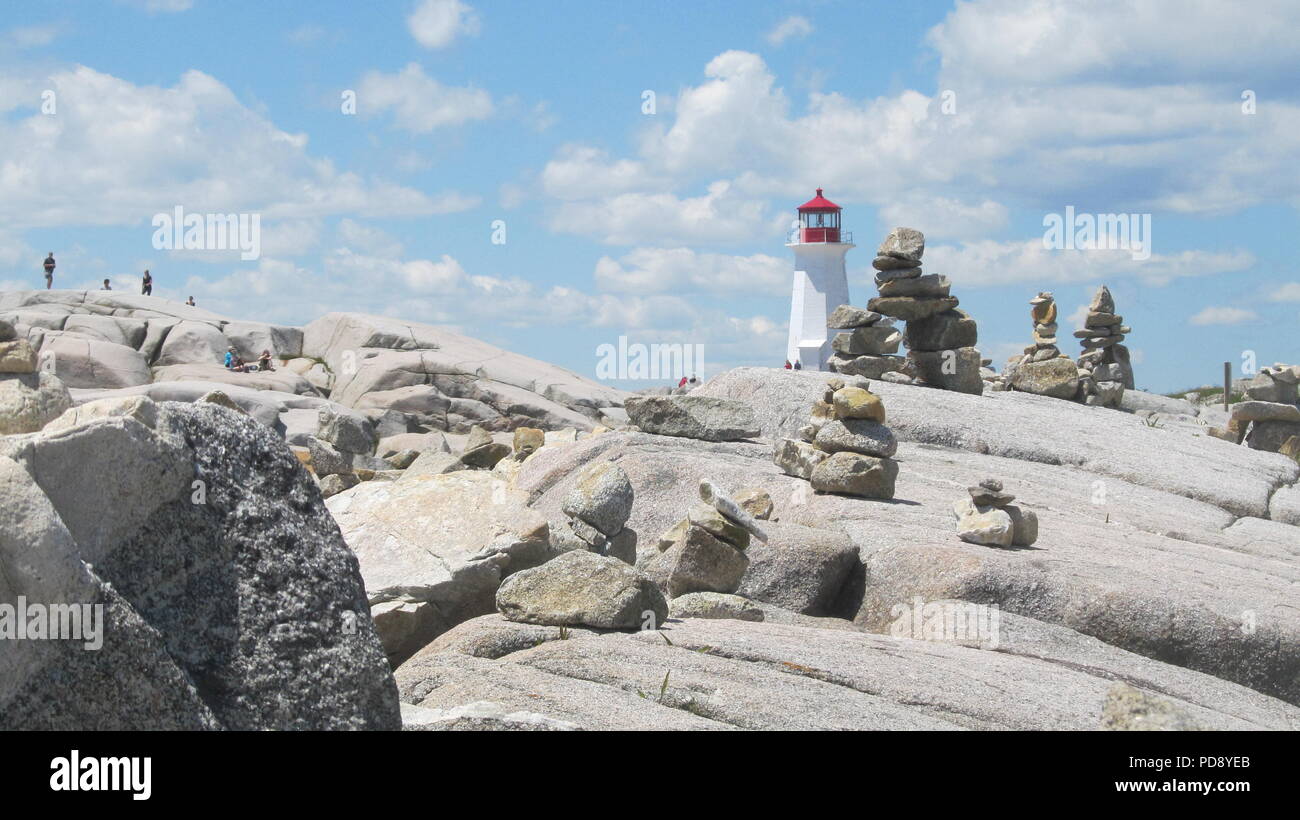 Peggy's cove lighthouse in Canada surrounded by rocks inukshuks and tourists Stock Photo