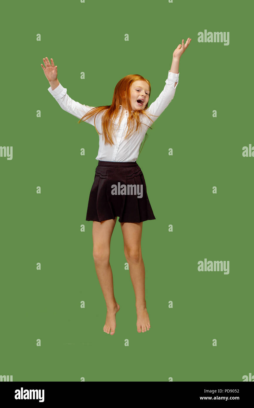 Young happy caucasian teen girl jumping in the air, isolated on green studio background. Beautiful female half-length portrait. Human emotions, facial expression concept. Stock Photo