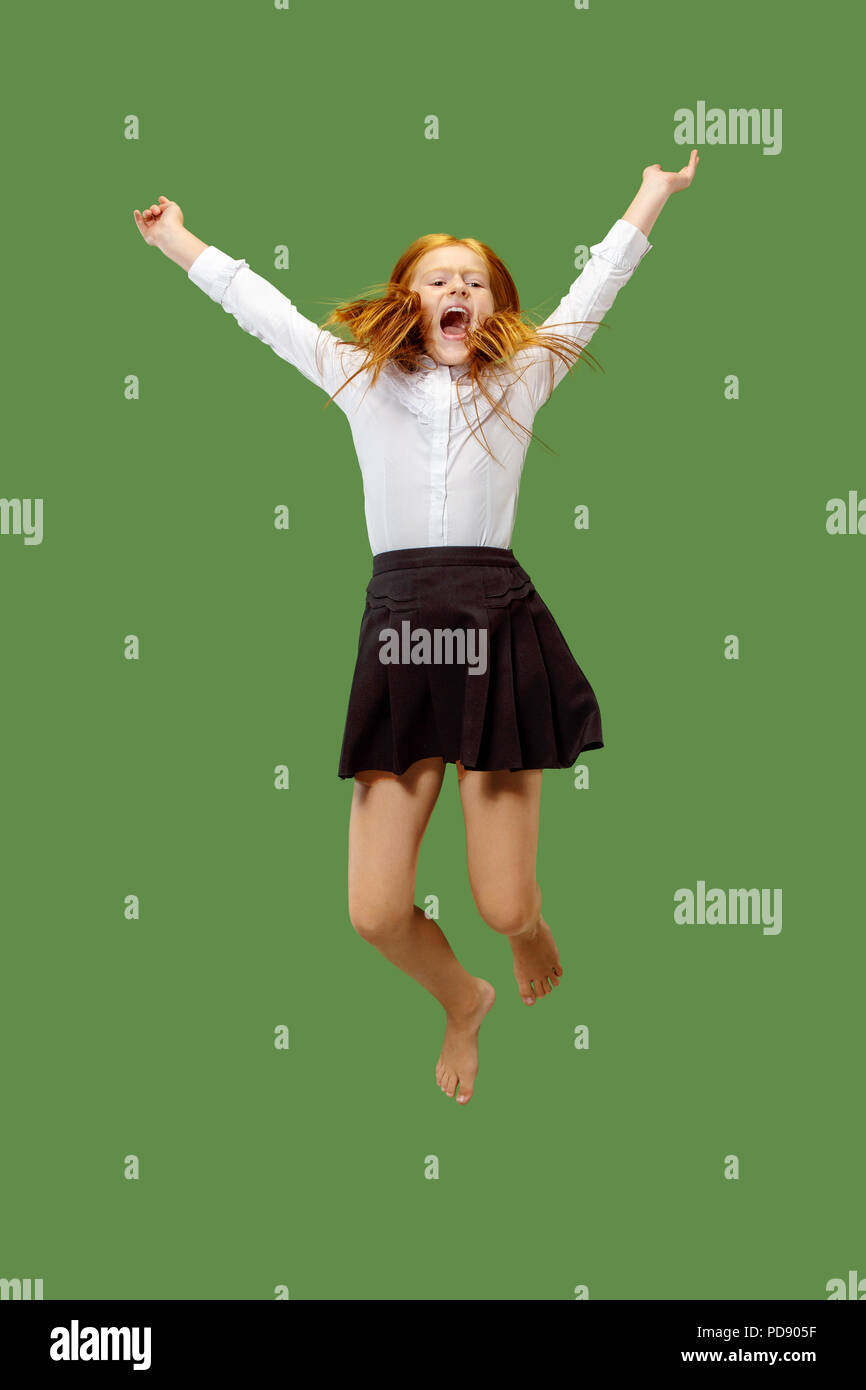 Young happy caucasian teen girl jumping in the air, isolated on green studio background. Beautiful female half-length portrait. Human emotions, facial expression concept. Stock Photo