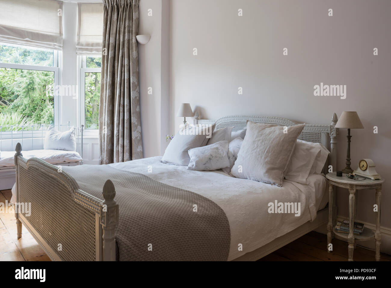 French antique rattan bed in bedroom with bed linen from House of Fraser. The cushions come from the White company Stock Photo