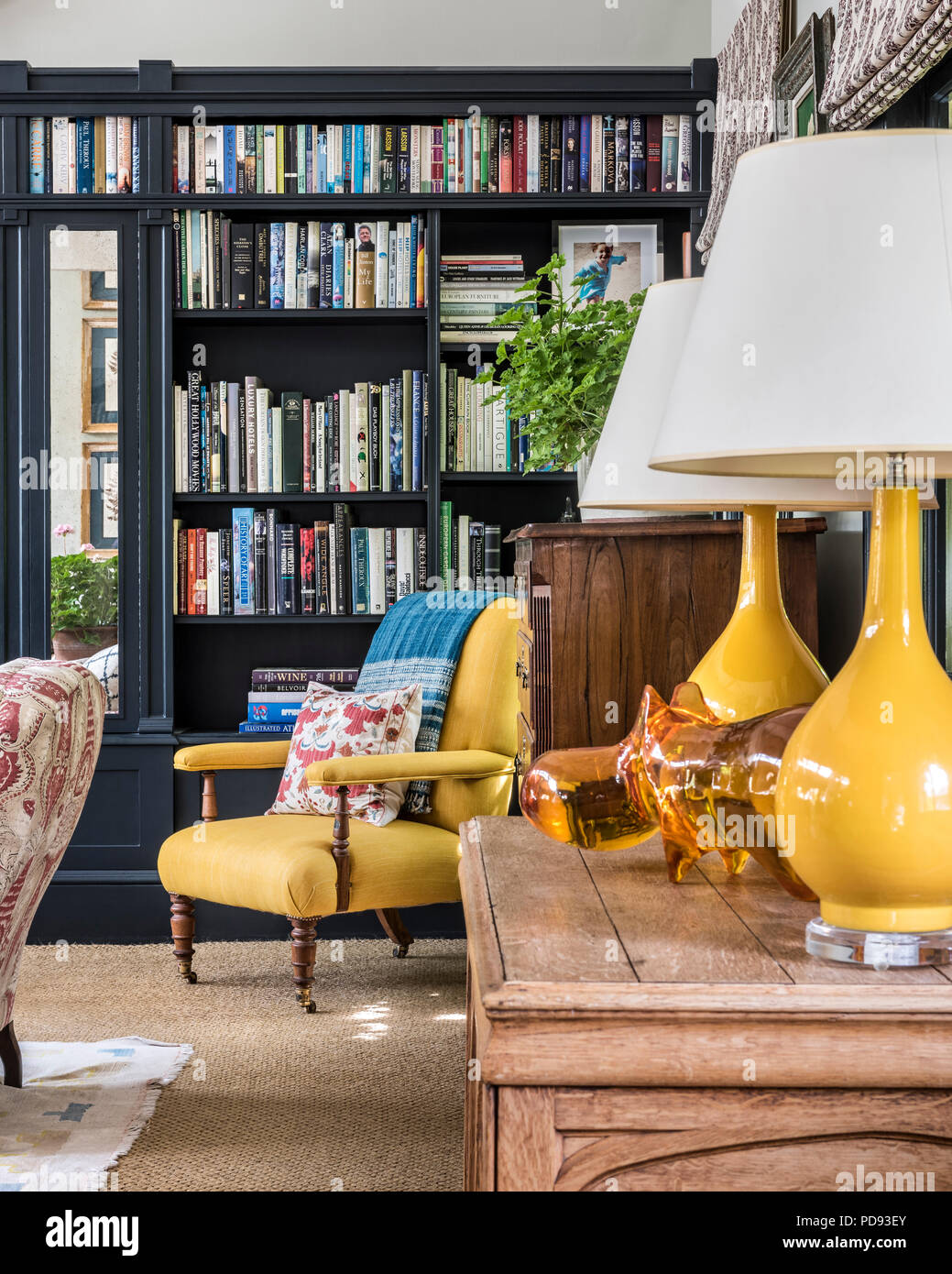 Yellow Fermoie linen on a C1900 chair matches a pair of yellow lamps from Tyson. The chair cushion is a Suzani textile while the resin Hippo between t Stock Photo