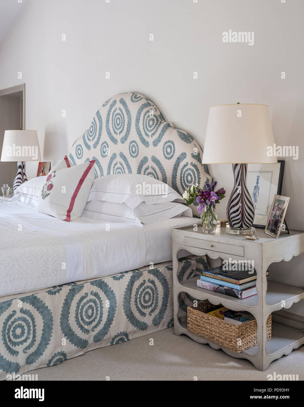 The custom-made curvy head board is covered in a Penny Morrison, blue and white printed linen, Haveli Blue. The elegant, purple stripey glass lamps ar Stock Photo