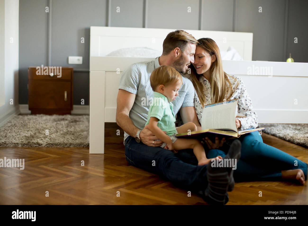 Young parents reading book to little boy and have fun on the floot in the room Stock Photo