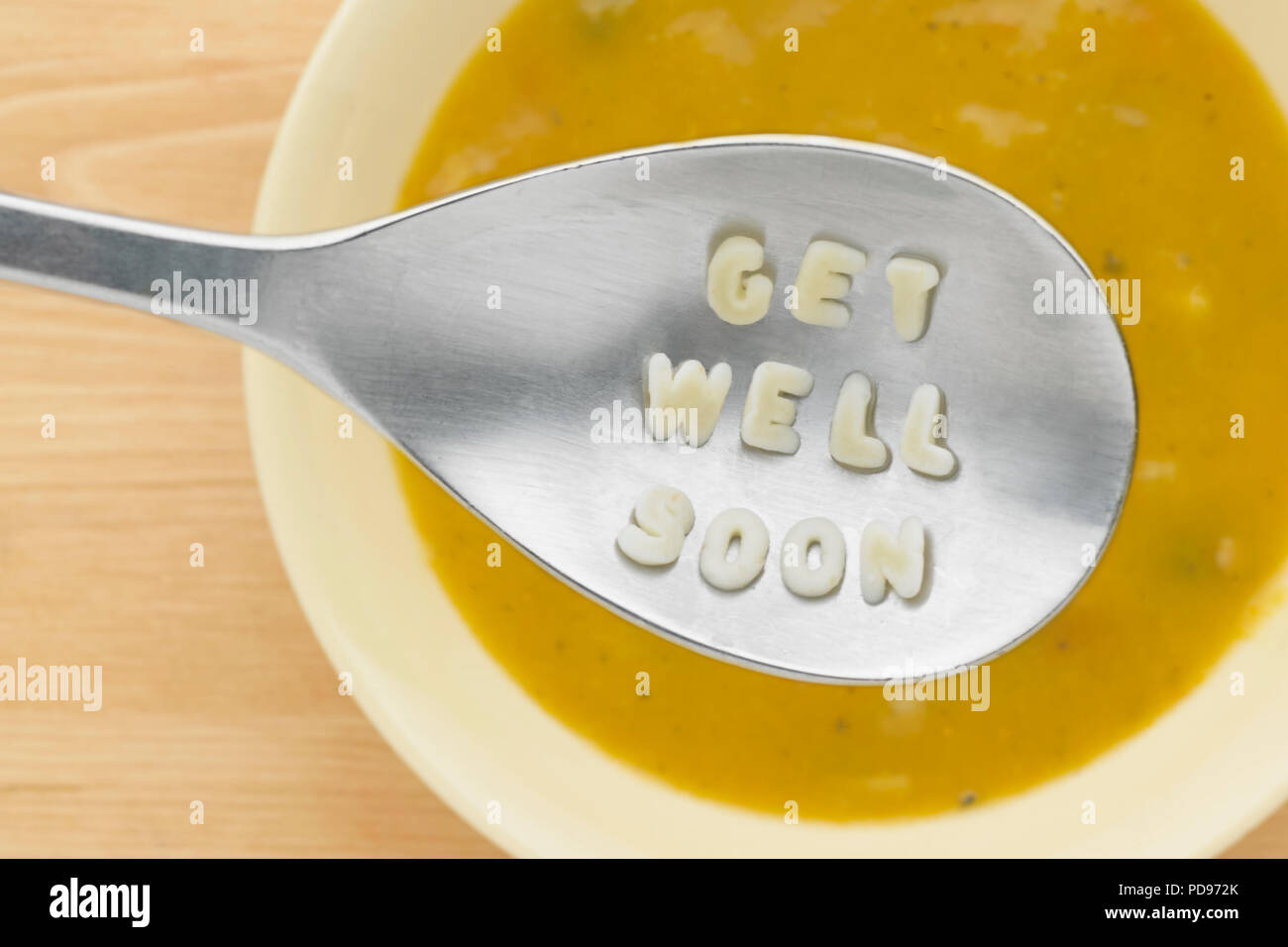 'Get well soon' in pasta shapes on spoon over bowl of soup Stock Photo