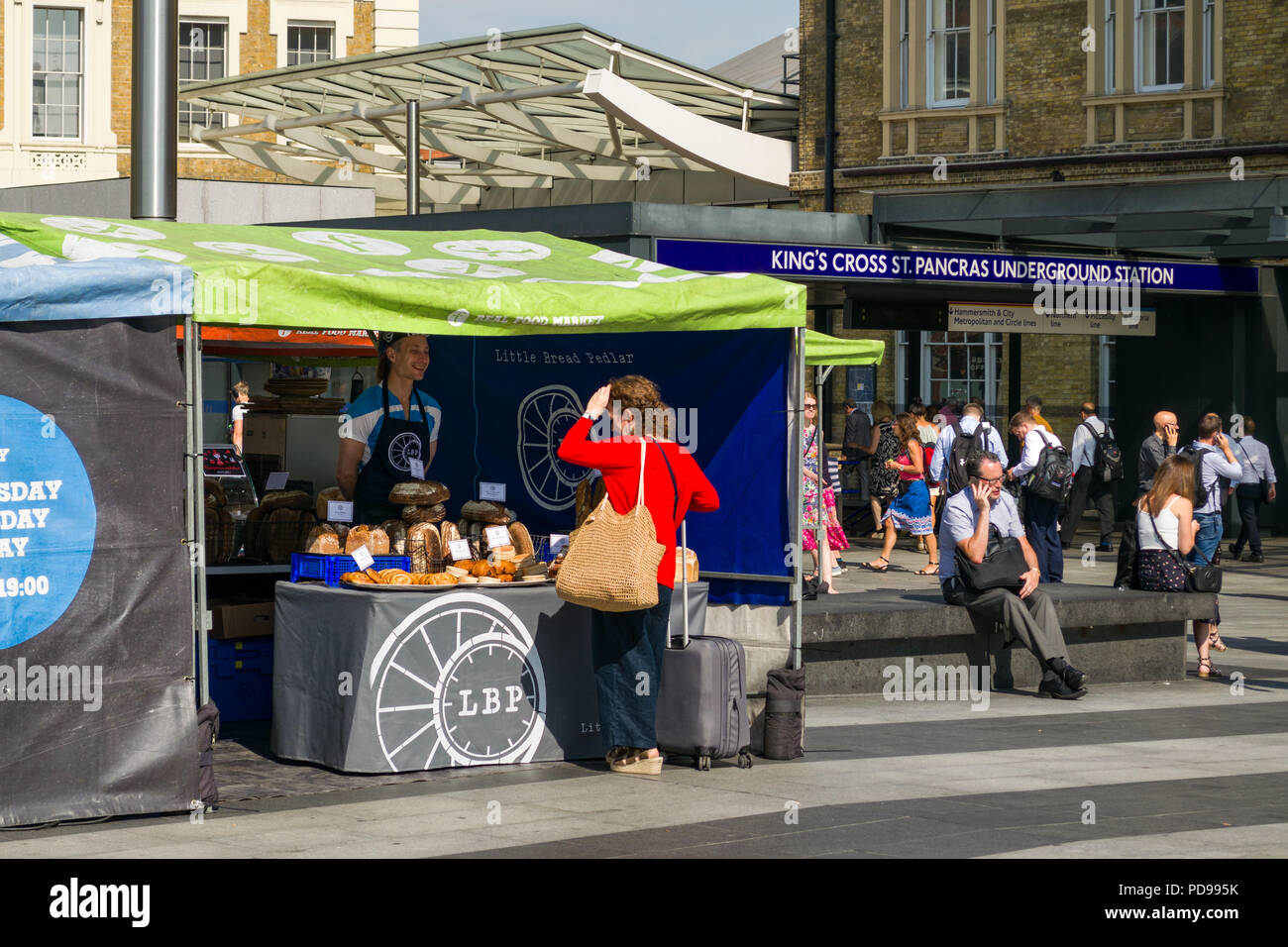 A small artisan bread and baked goods market stall with woman browsing goods on display outside Kings Cross train station, London, UK Stock Photo