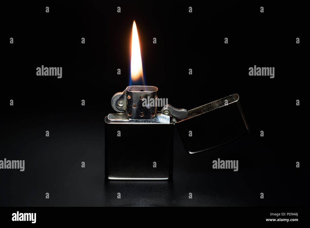 Shiny silver metallic lighter with lit flame of fire on a black background. Stock Photo