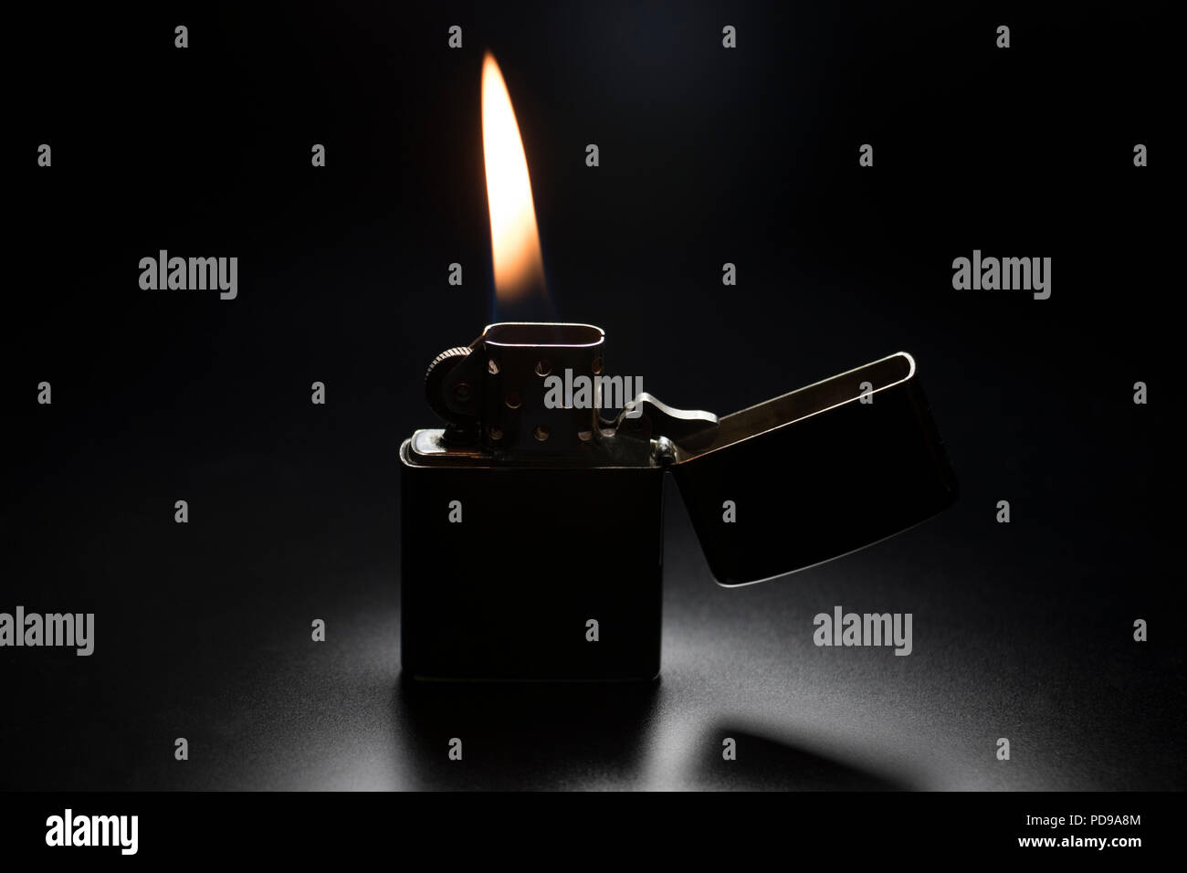 Lighter lit with yellow flame on black background. Vintage stainless steel cigarette lighter with spring flip lid. Stock Photo