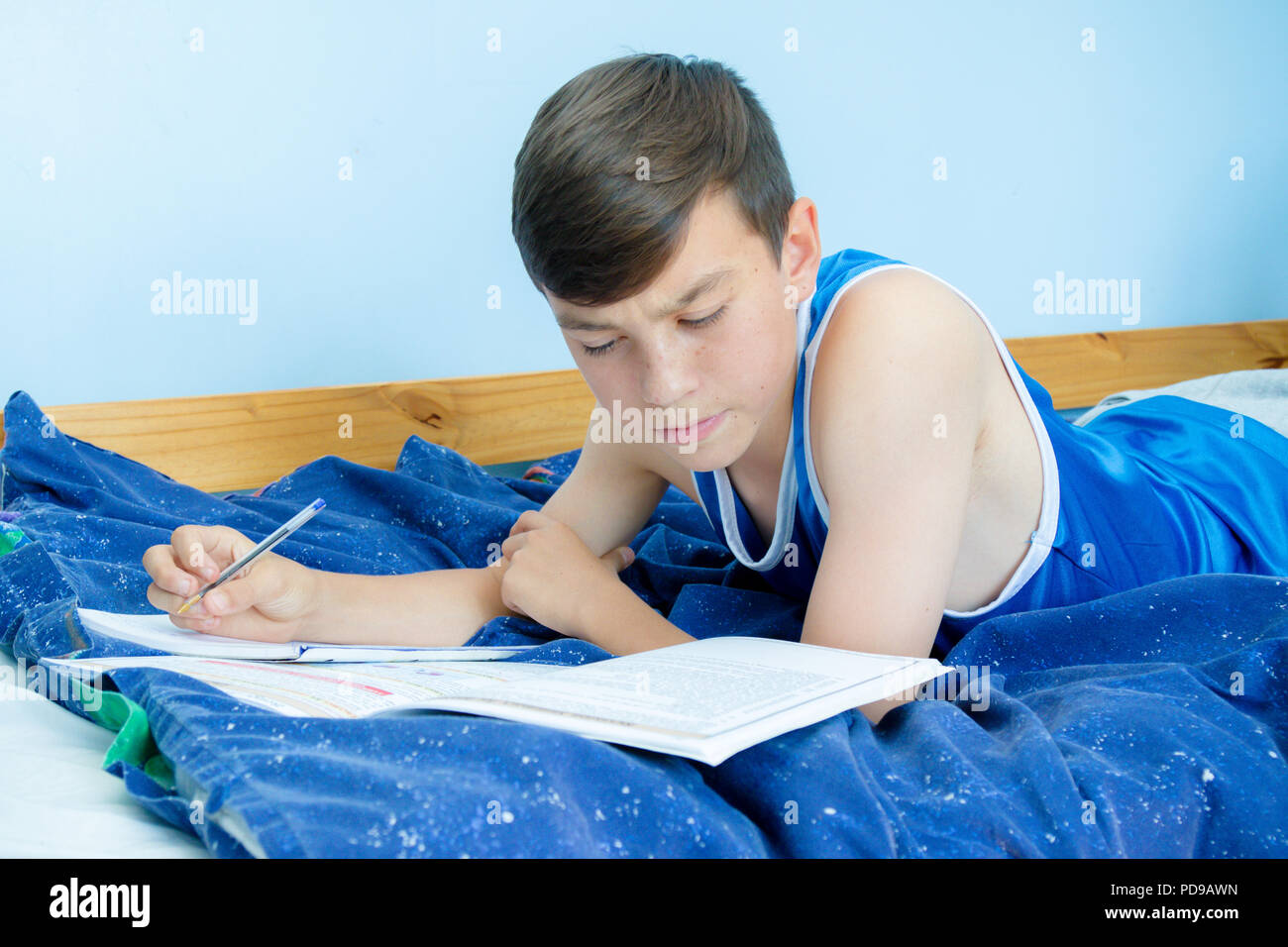 caucasian-teenage-boy-laying-on-his-bed-reading-a-textbook-stock-photo