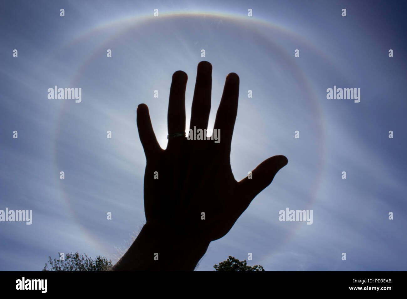 Stockholm, Sweden - August 6 2018: Circular rainbow around the sun which is blocked by the hand of a young male. Meteorological phenomenon. Stock Photo