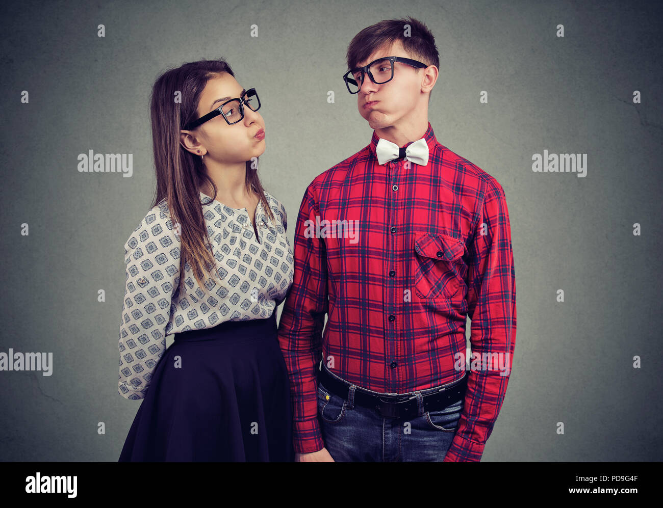 Young man and woman in couple making expression of disagreement and offense while looking at each other on gray background Stock Photo