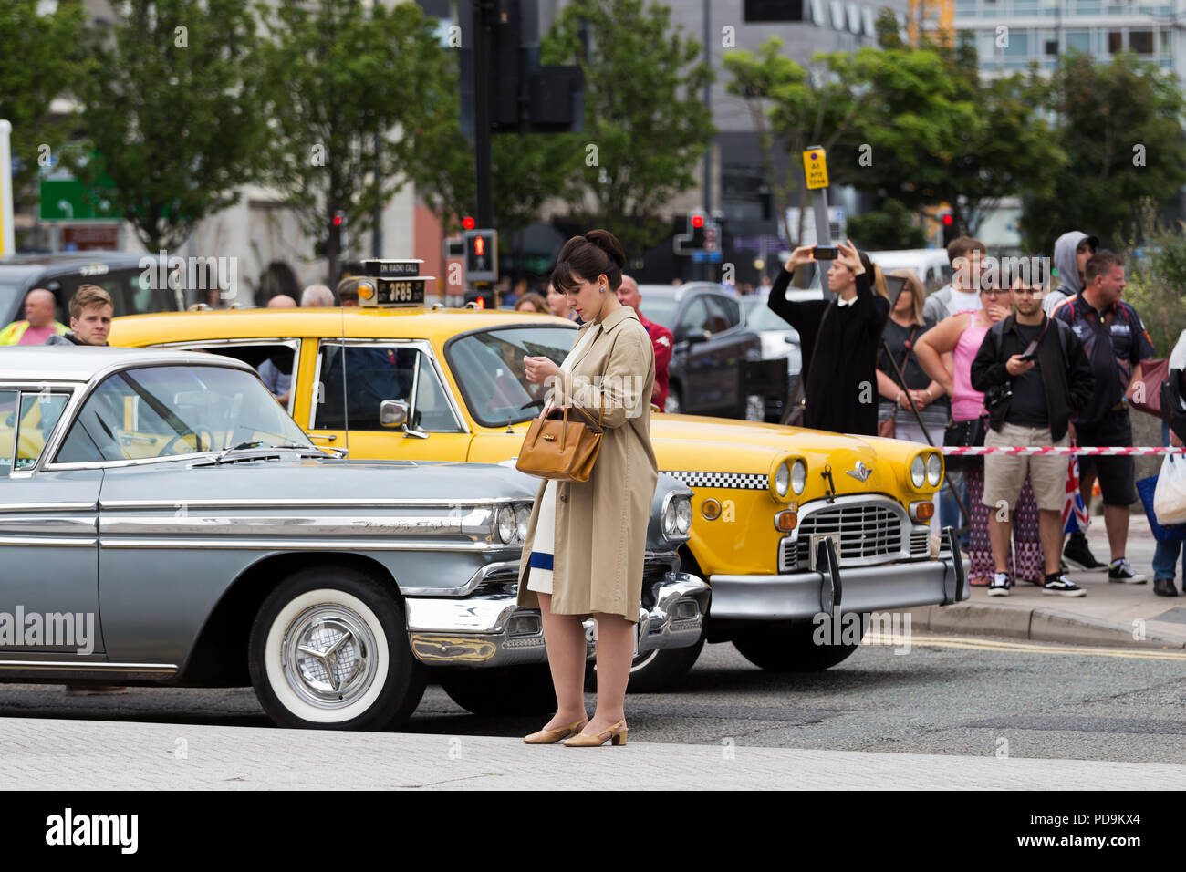 A female extra dressed in 1960s clothing stands in front of a vintage Washington DC yellow taxi cab  whilst being filmed as part of a major TV series. Stock Photo