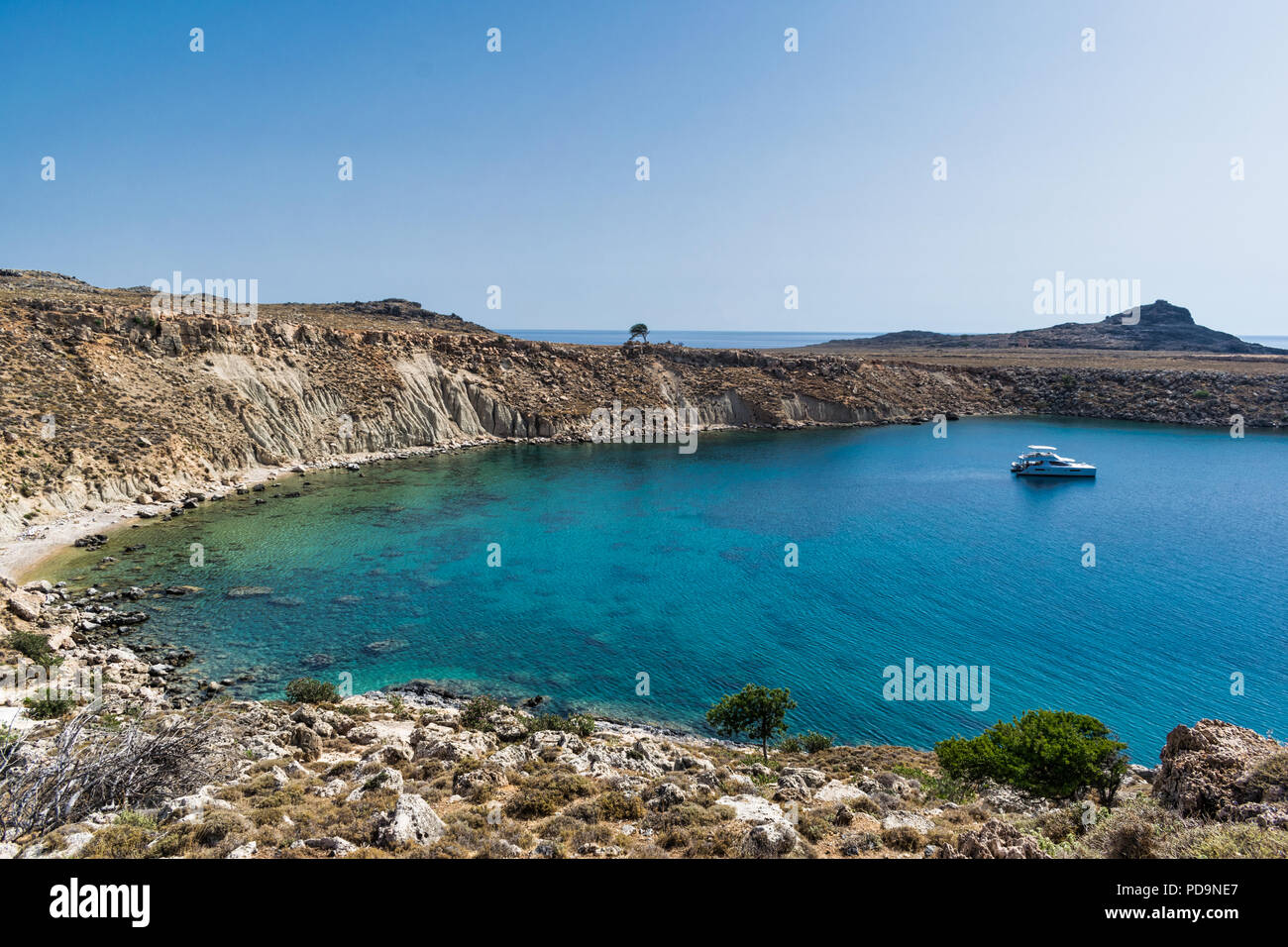 This is a remote harbour near Lindos Greece on the Island of Rhodes.  The water is turquoise blue with a single achord motor boat Stock Photo