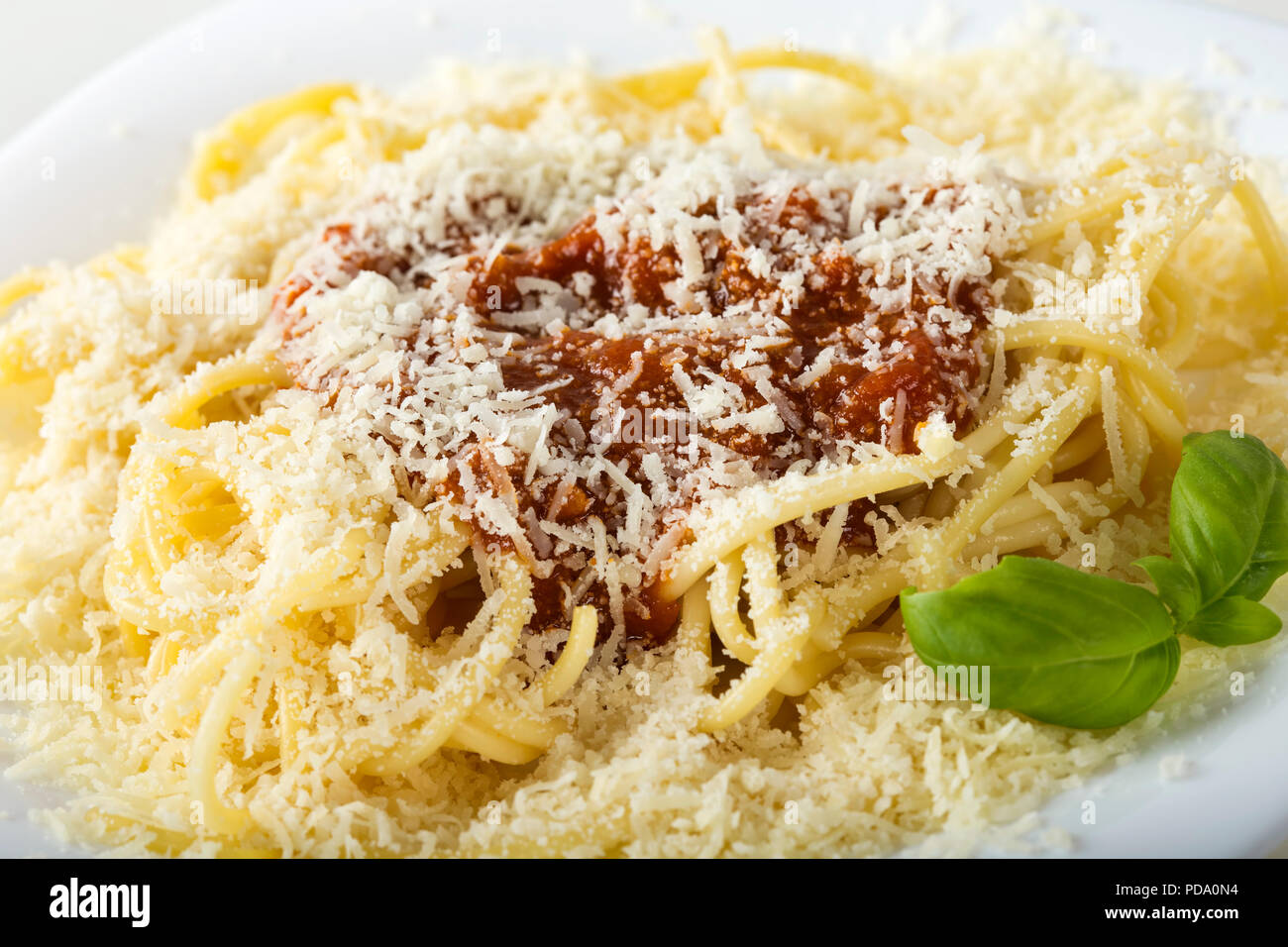 Spaghetti bolognese with a lot of parmesan cheese on a white plate