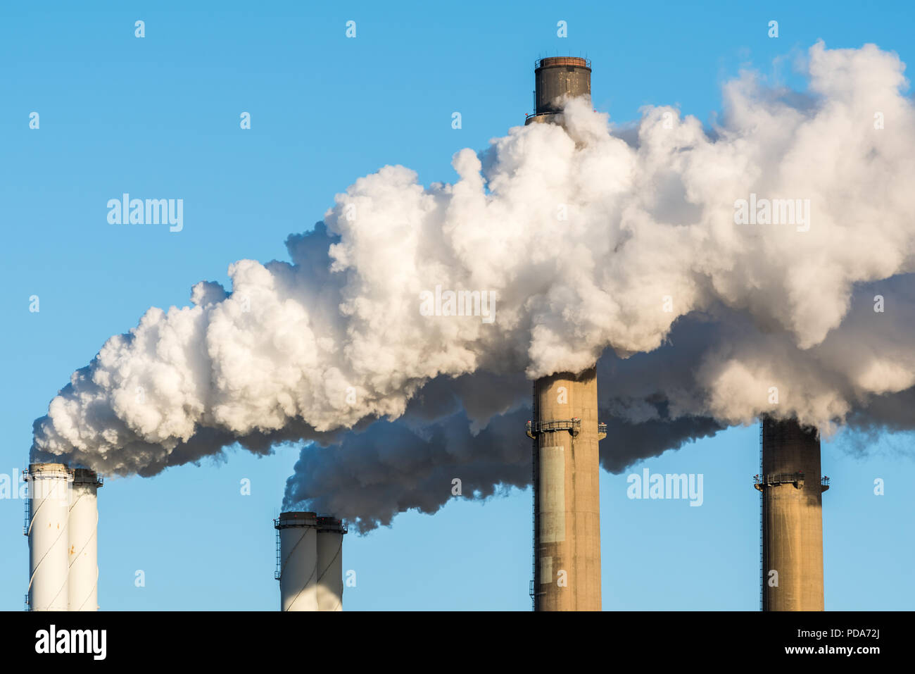 The chimneys of a powerstation with huge smoke stacks and a blue sky as background. Stock Photo