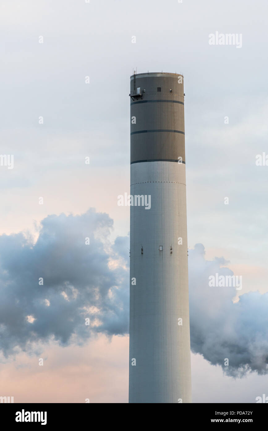 Close up of a chimney of a coal power plant during sunset. A smoke stack from another pipe is in the background against the slightly colored sky. Stock Photo