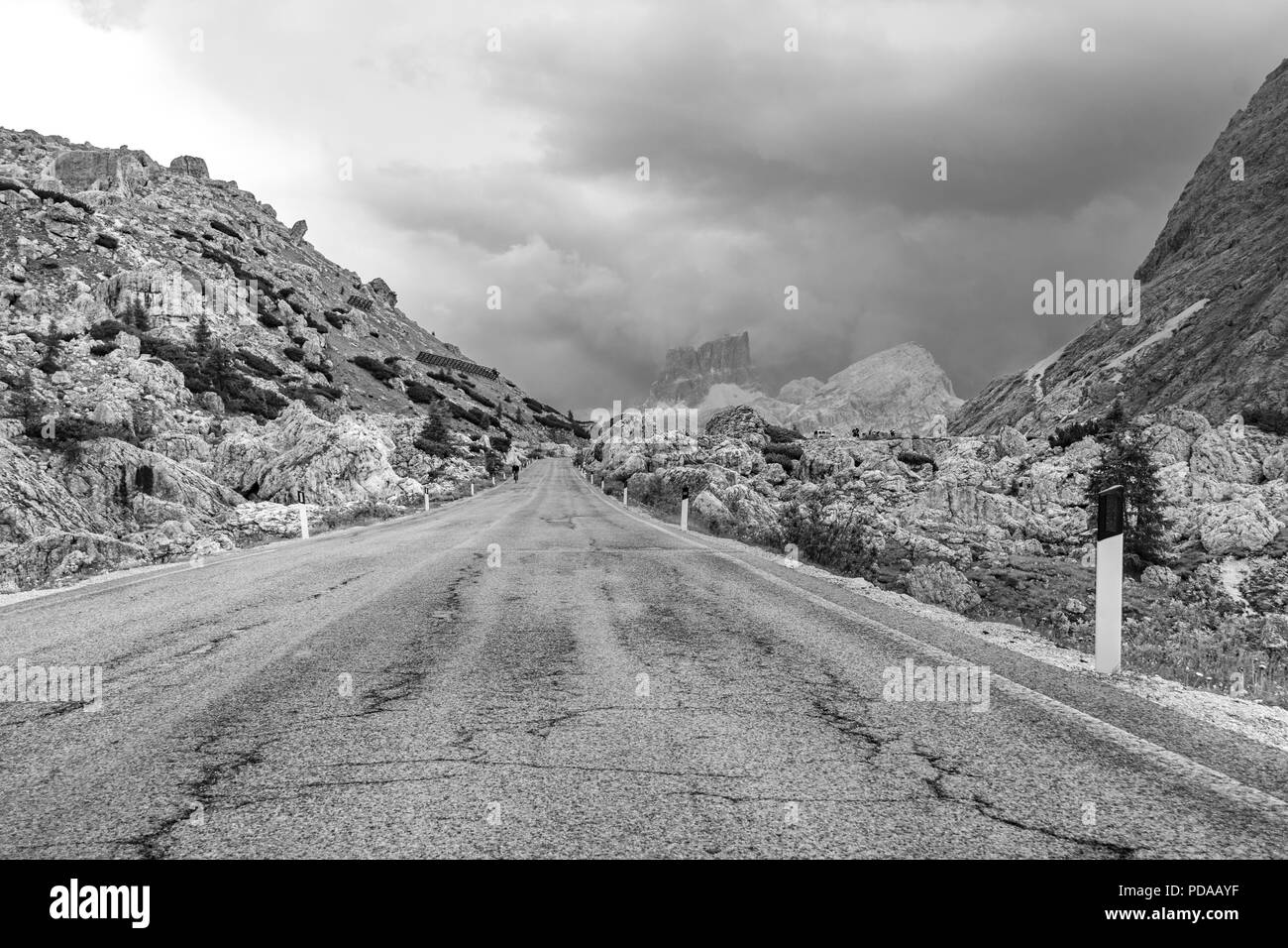 Empty deserted road in black and white leading to menacing stormy, cloudy mountains in the Dolomites, Italy Stock Photo