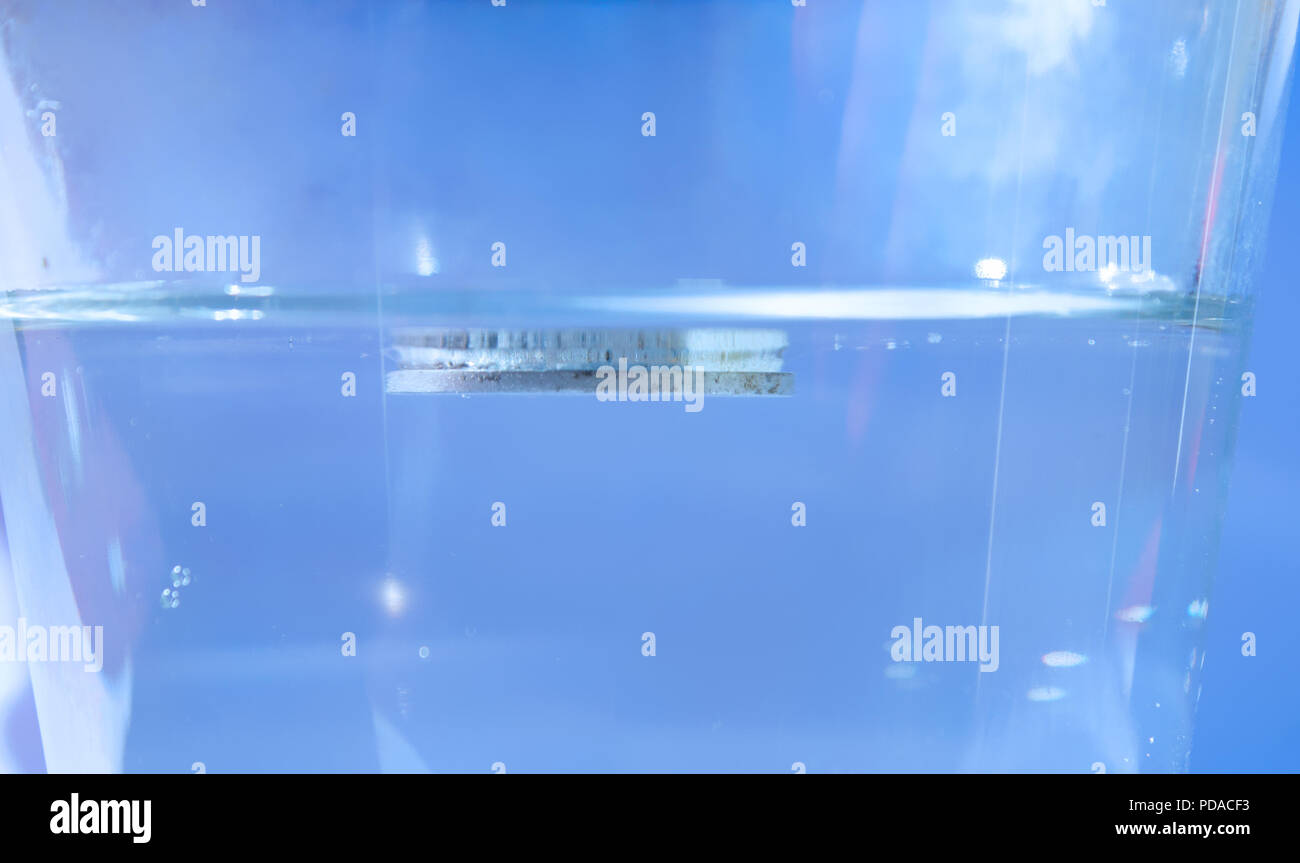 The isolated coin in a glass of water floats on the water surface