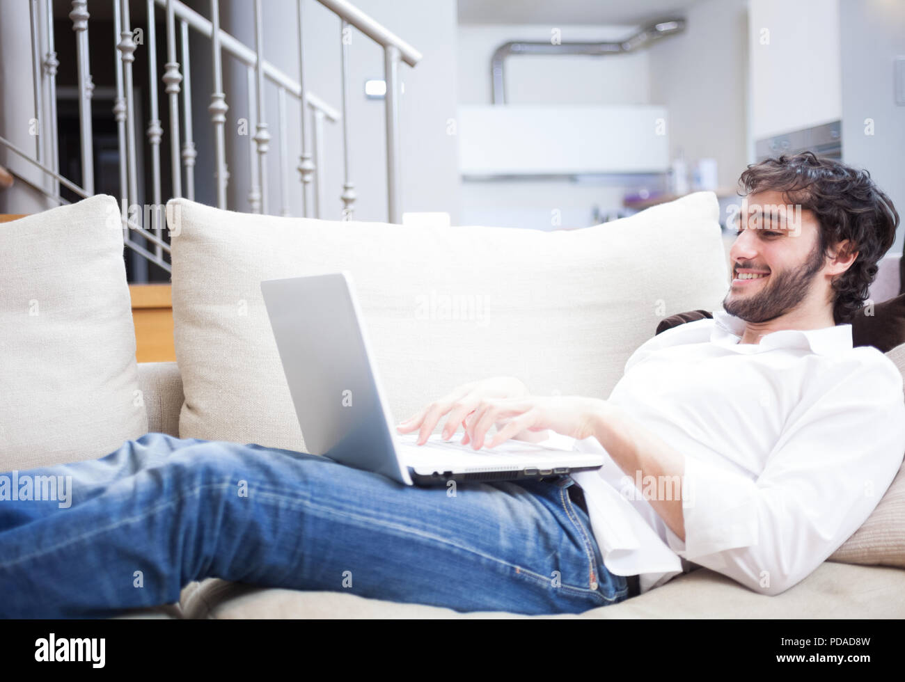 Man using a laptop computer while lying down on the couch in his living room Stock Photo Alamy