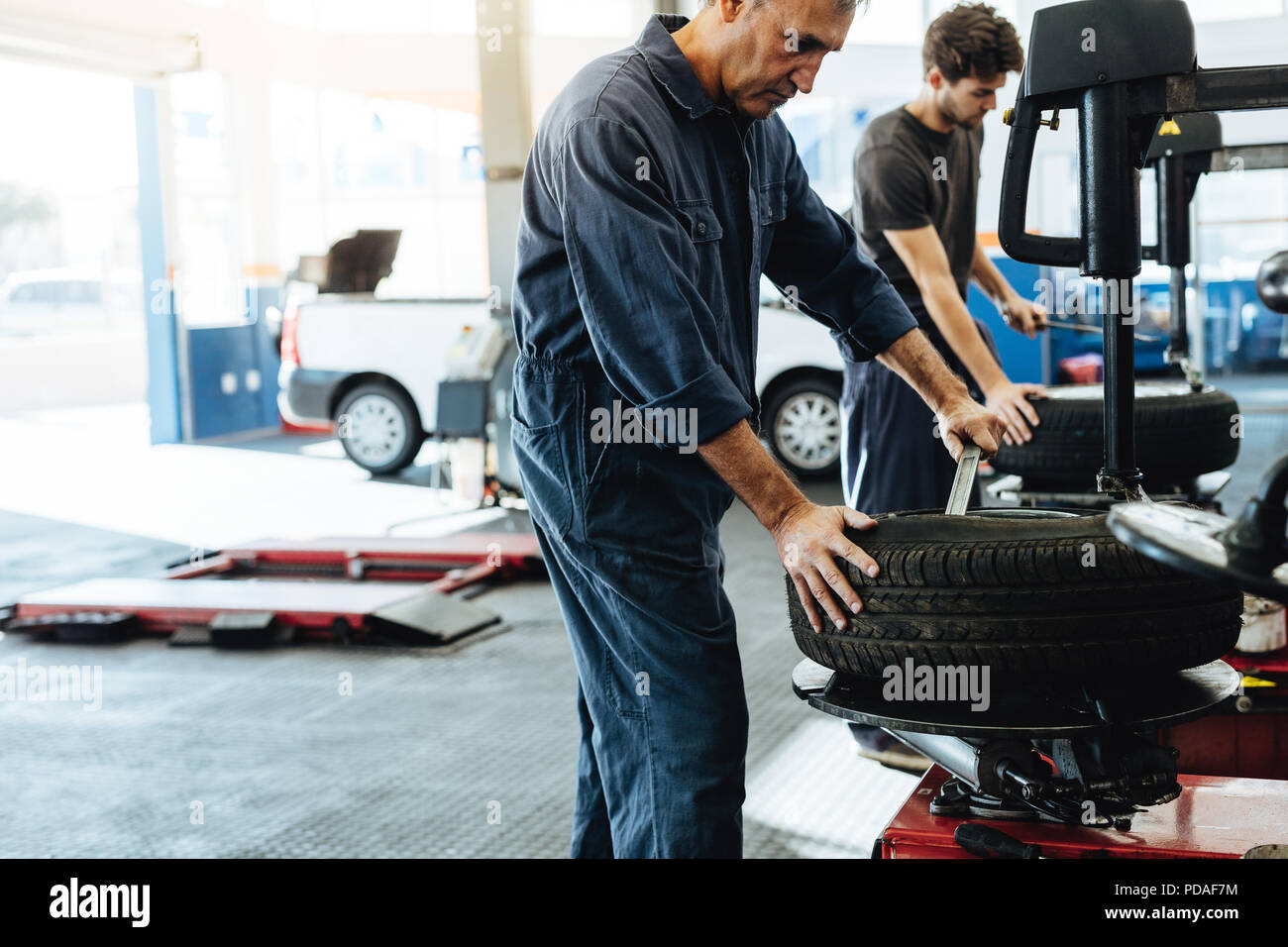 Mechanics working in car repair workshop. Auto repair workers working on tire replacing machine in auto repair shop. Stock Photo