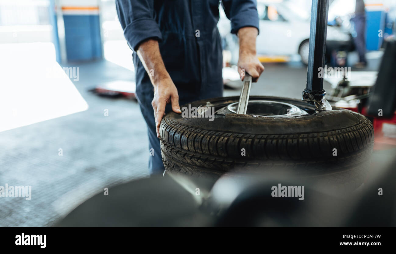 Hands of mechanic removing car tire from disc on machine. Man working on machine for removing rubber from the rim in auto repair shop. Stock Photo