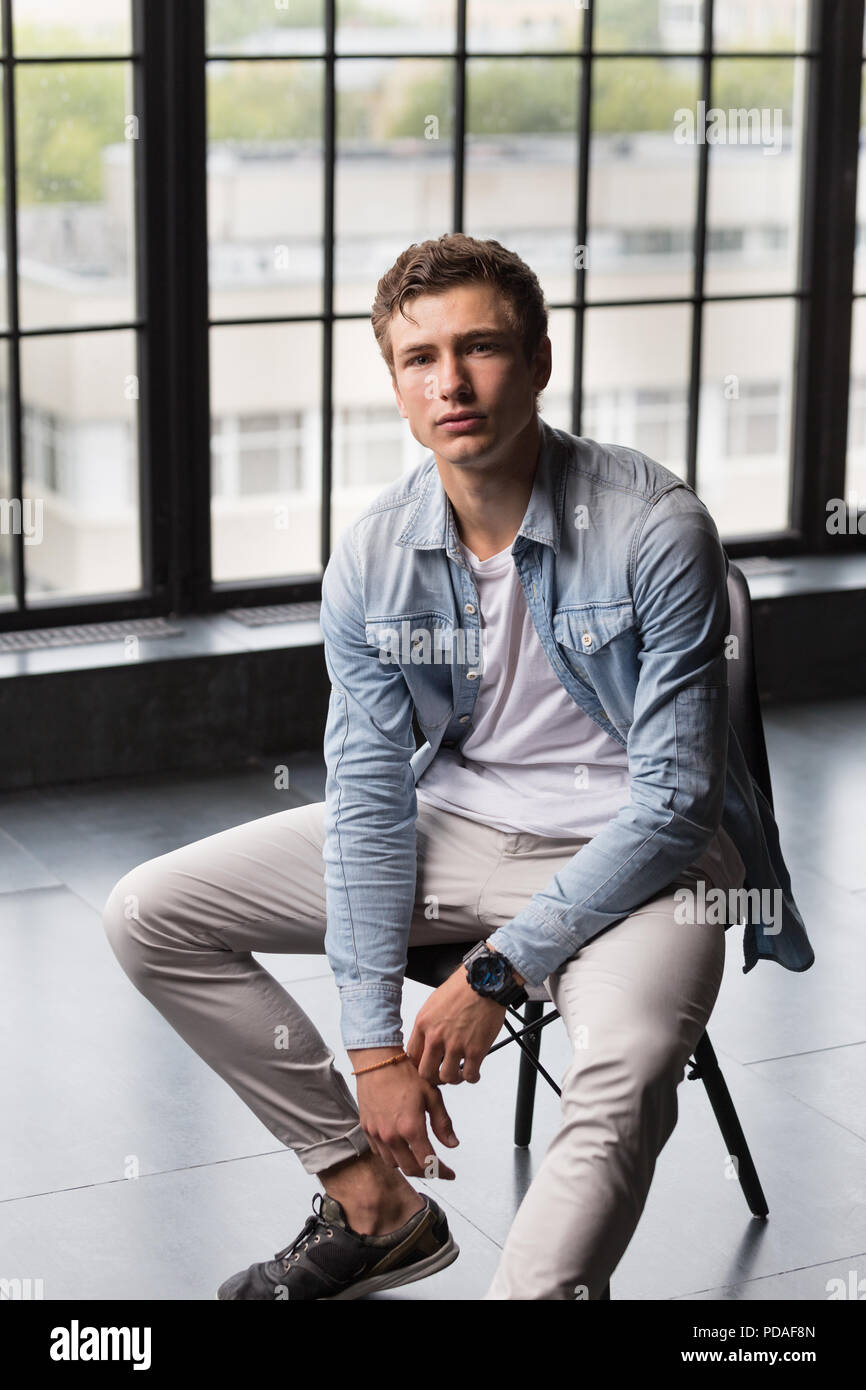 Handsome young male model in blue shirt and white pants at modern interior photostudio Stock Photo