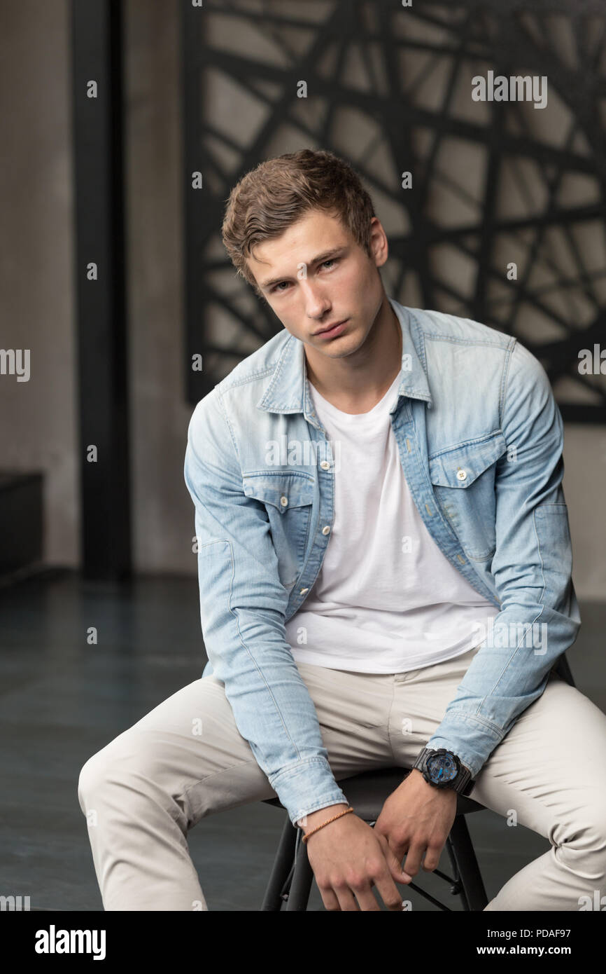 Handsome young male model in blue shirt and white pants at modern interior photostudio Stock Photo