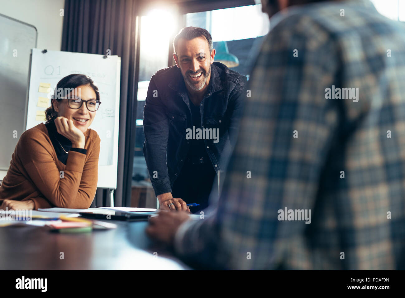 Smiling business people paying attention to colleagues discussion in meeting room. Happy and positive business team meeting in conference room. Stock Photo