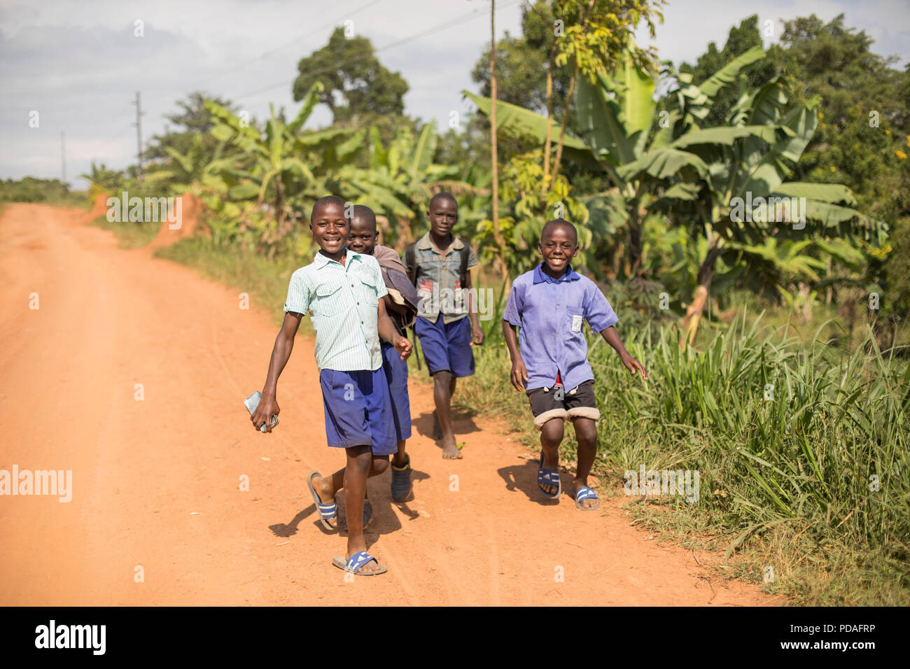 Happy school children run down a dusty road in Mukono District, Uganda. Stock Photo