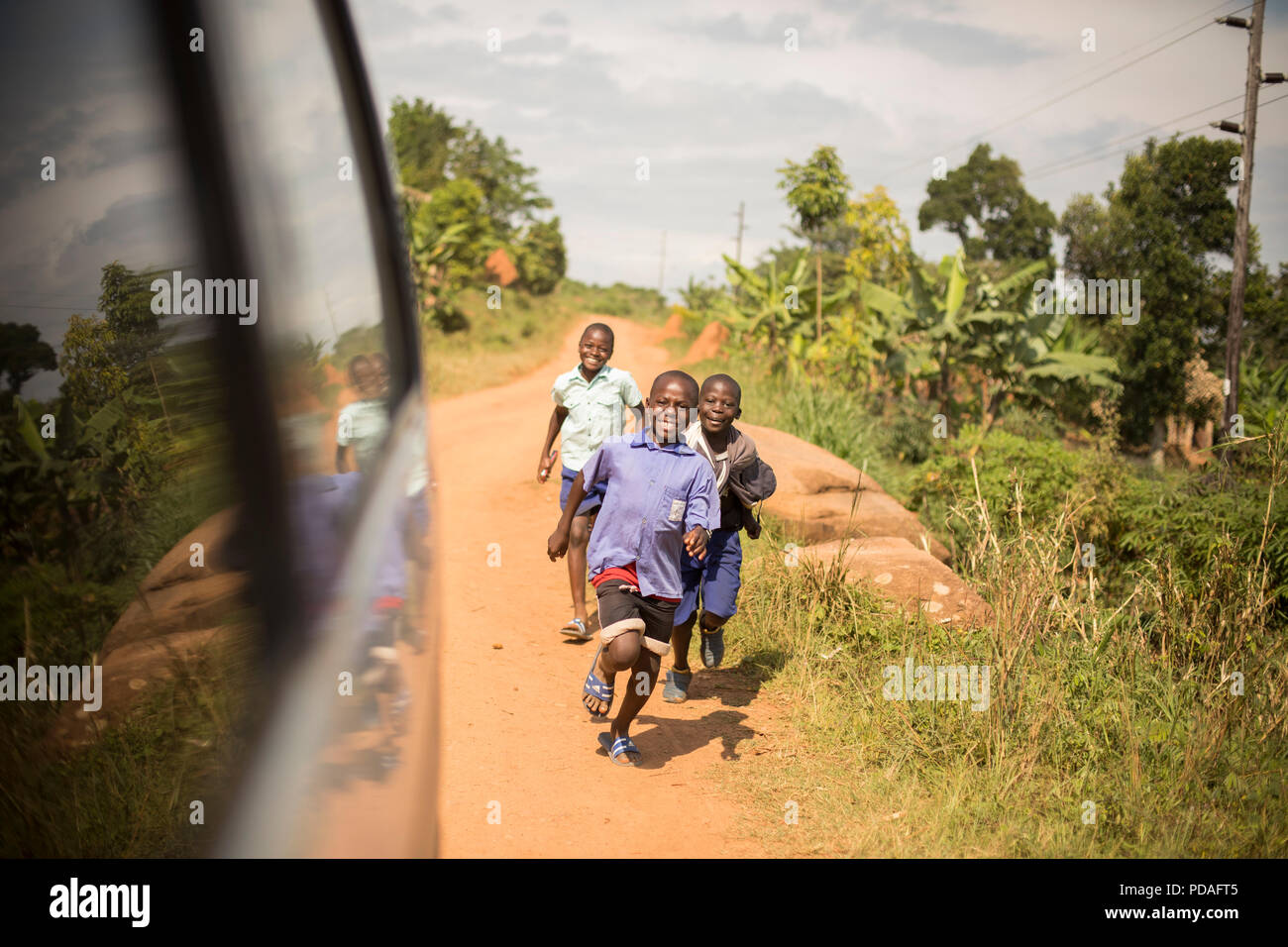 Happy school children run down a dusty road in Mukono District, Uganda. Stock Photo