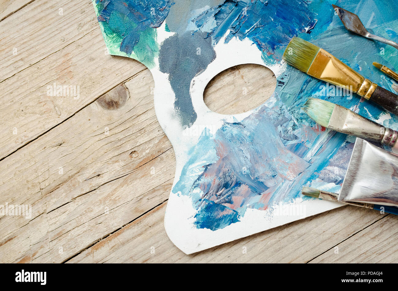 Artist paint brushes and oil paint tubes on wooden palette. Texture mixed oil paints in different colors. Instruments and tools for creative leisure.  Stock Photo