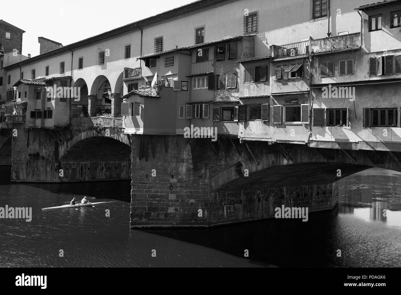 Close-up of the Ponte Vecchio spanning the River Arno in Florence Tuscany, Italy, with a double scull shooting the bridge.  Black and white version Stock Photo