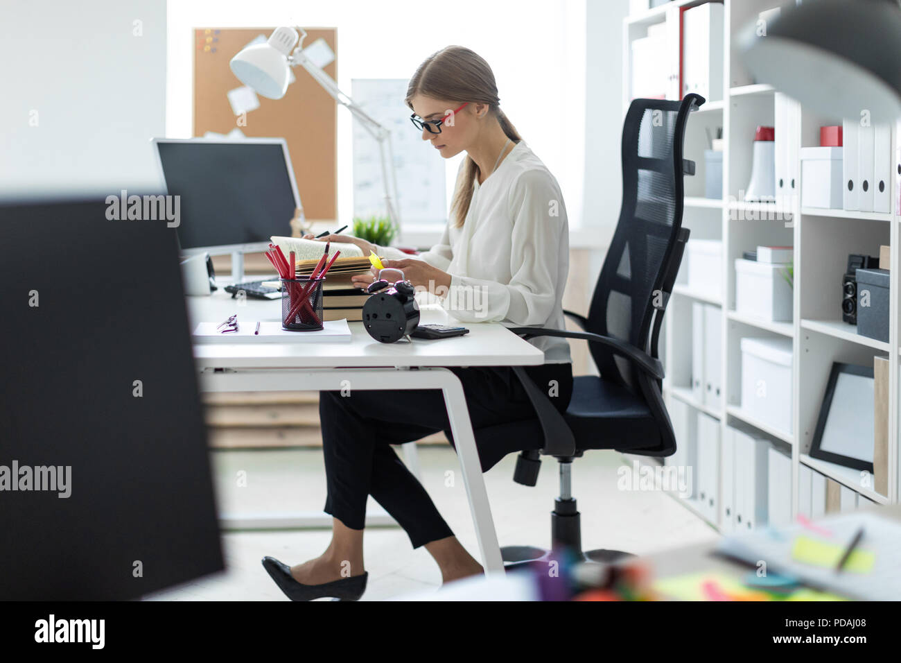 A young girl sits at a table in the office and holds a yellow marker in